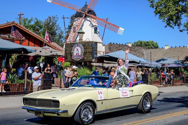 A woman sits atop a convertable with a windmill in the background at a parade in Solvang. 