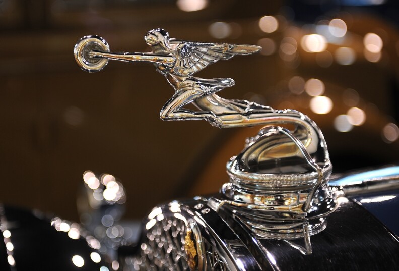 A radiator cap of a 1931 Packard, 845 Deluxe Eight, Sport Sedan, looks like the Greek god Mercury with the arms reaching with a wheel at the end.
