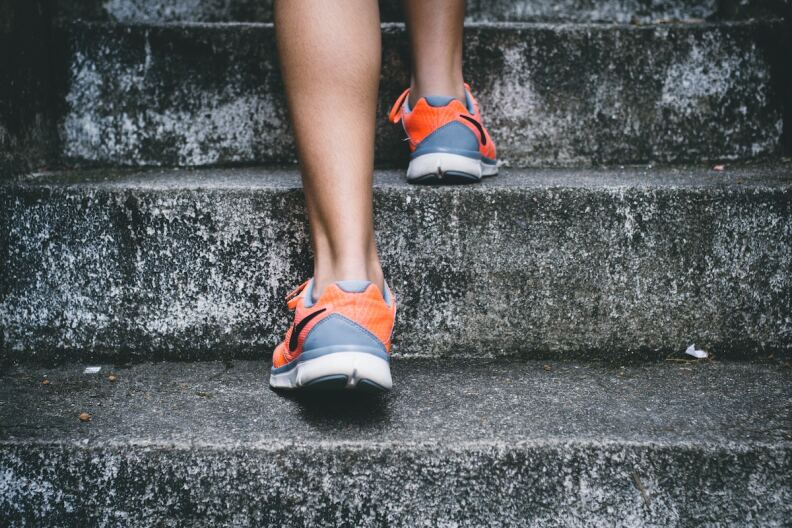 A person with gray and orange running shoes goes up stone steps.
