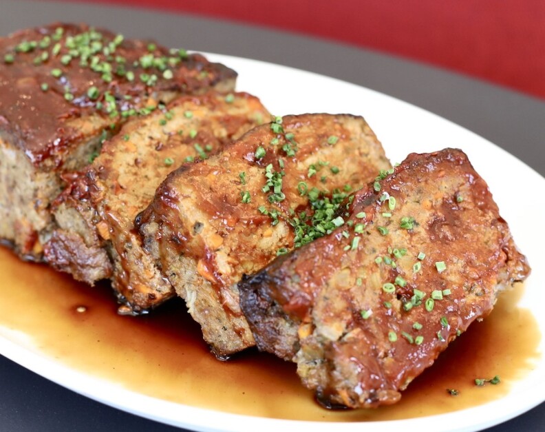 A meatloaf with three slices leaning over on a plate of au jus. 