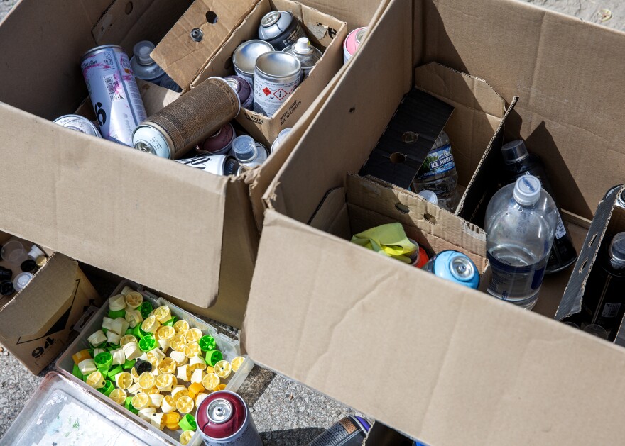 Cardboard boxes of spray paint bottles and bottles of water. 