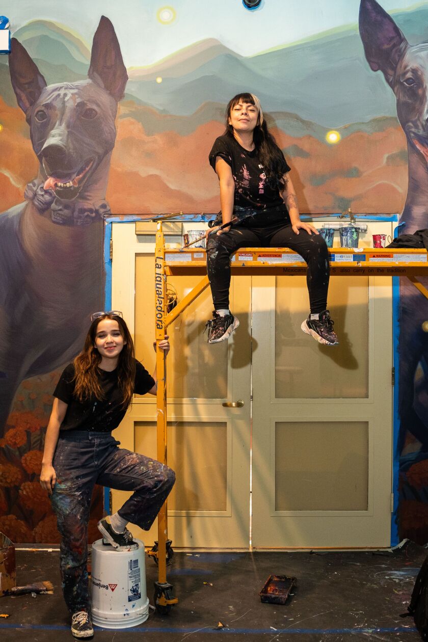 Visual artists Dolores “YUDA” Navarro (left) and Janín Garcín sit in front of a mural at the National Museum of Mexican Art in the Pilsen neighborhood, Wednesday, Sept. 19, 2023. The mural is part of the exhibit entitled, “Día de Muertos, Living Presence.”
