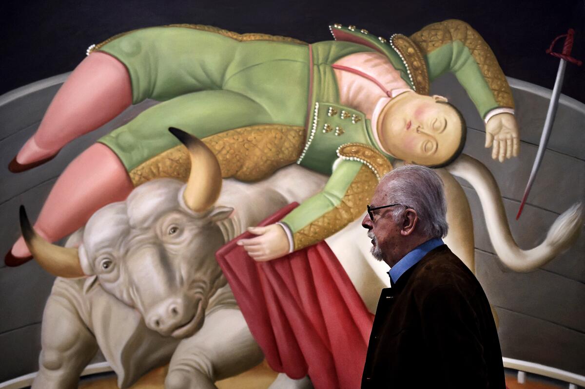 Fernando Botero stands next to one of his paintings, showing a matador with a bull.