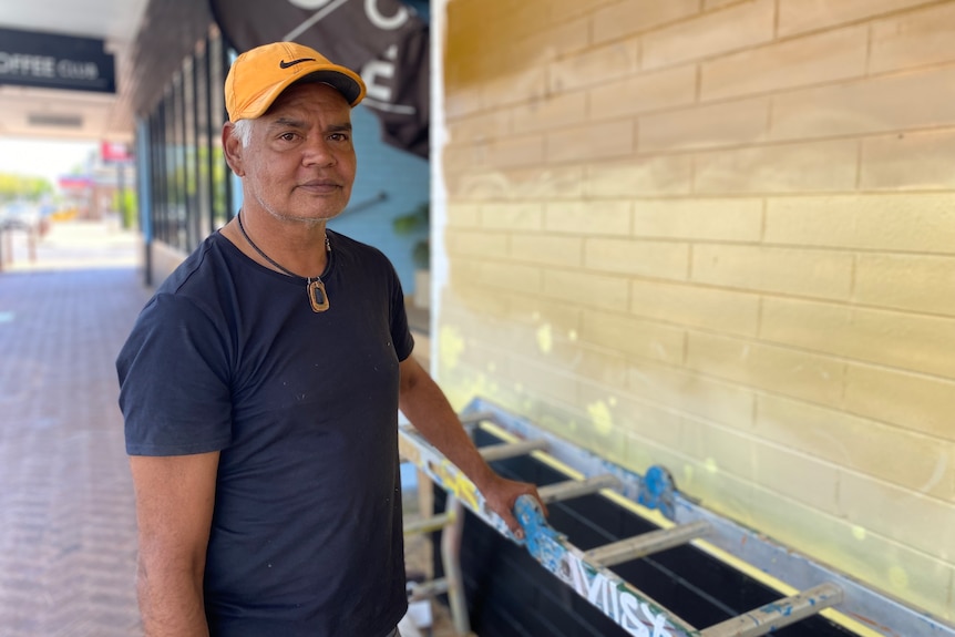 a man wearing a blue shirt and orange cap painting a wall