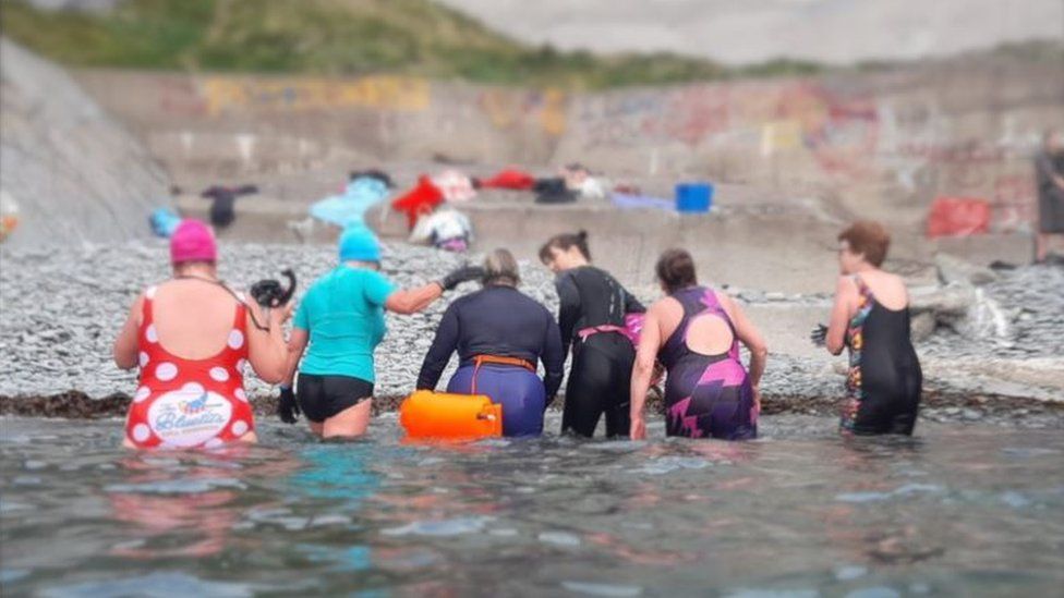 Manx Blutits swimmers in sea with graffiti in the background
