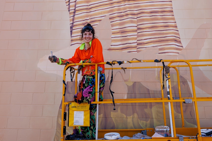 a young woman on a cherry picker painting a mural