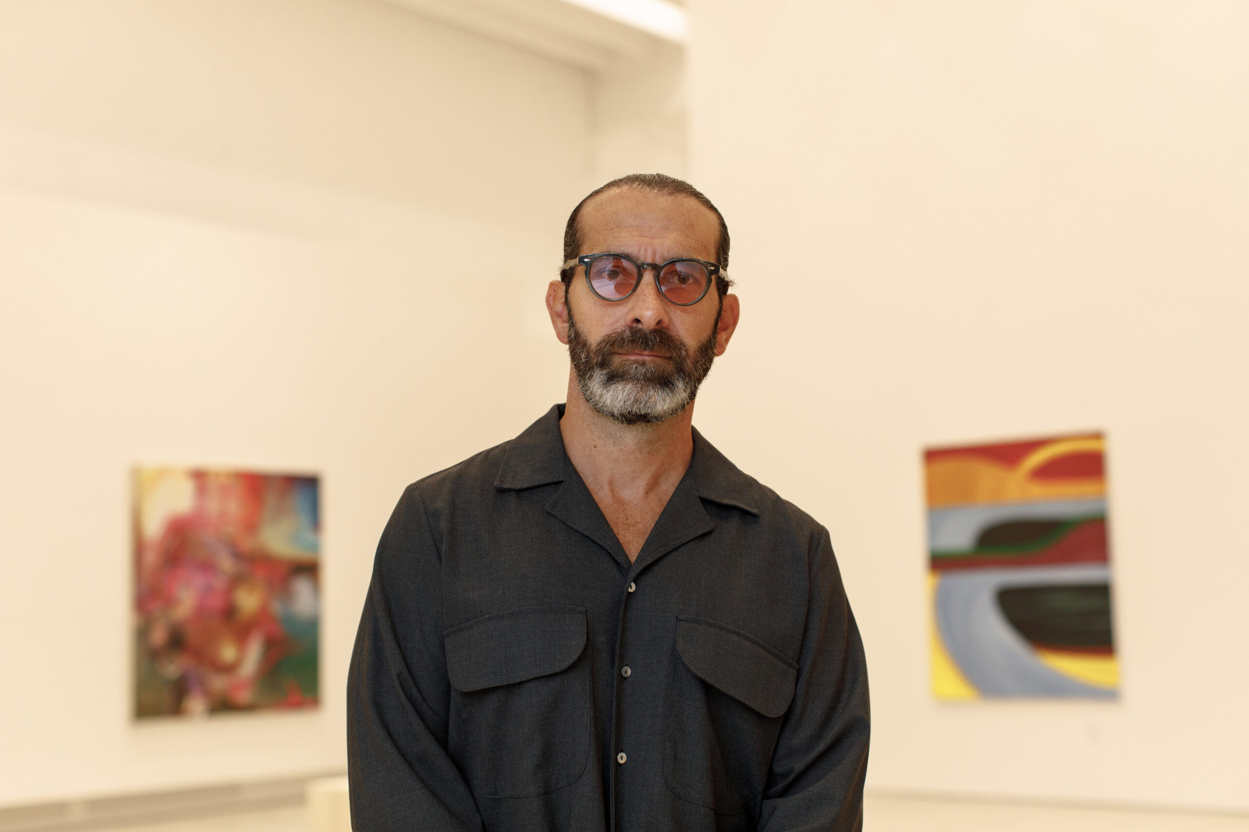 Man with grey beard and glasses standing in art gallery