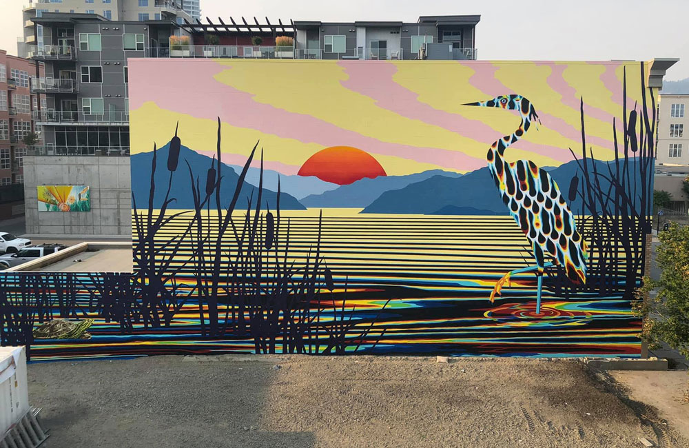 A wide shot of the heron mural, which is set against mountains and a setting sun