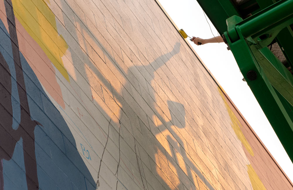 A student rolling paint onto the mural