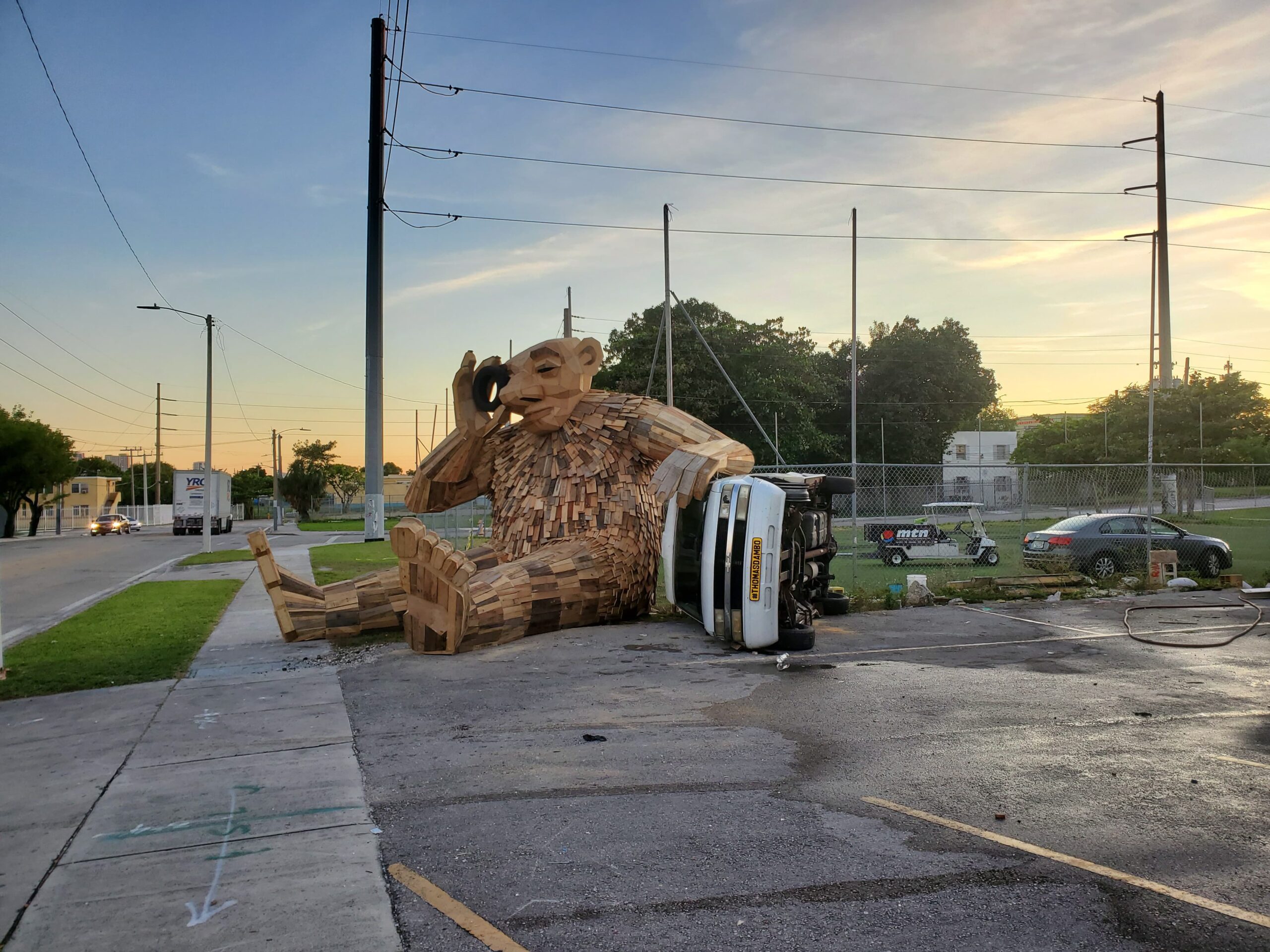 A giant wooden troll statue rests an arm on a car