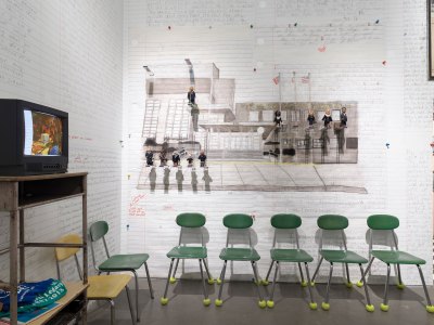 An installation showing people on diving boards made of erasers that are displayed over green school chairs on tennis balls. At right is an old-school TV. 