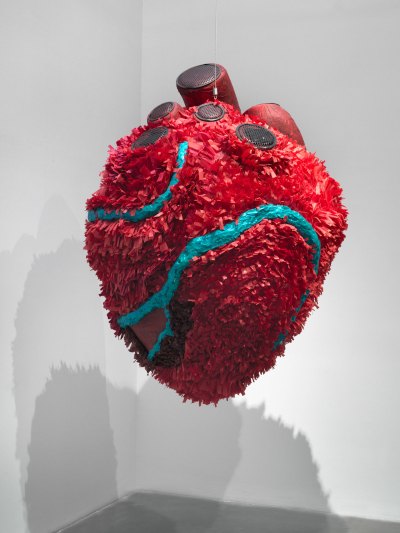 A six-foot sculpture of a heart that is decorated like a piñata with speakers on it. 