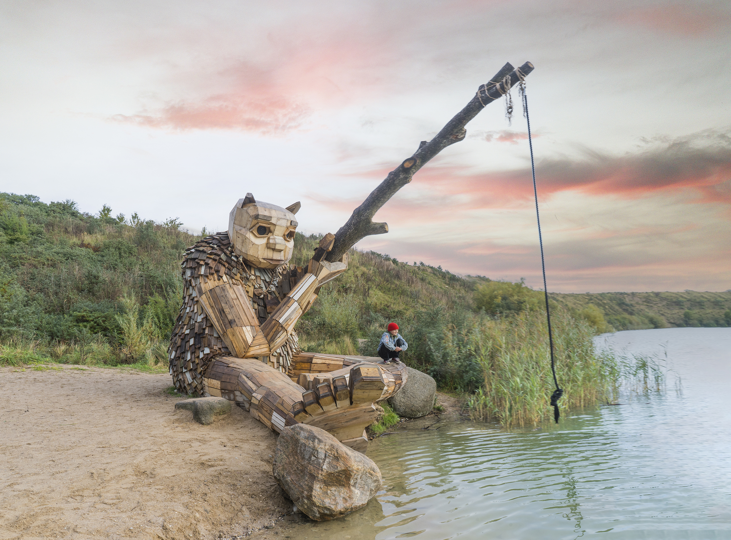A giant wooden troll statue fishes in a pond
