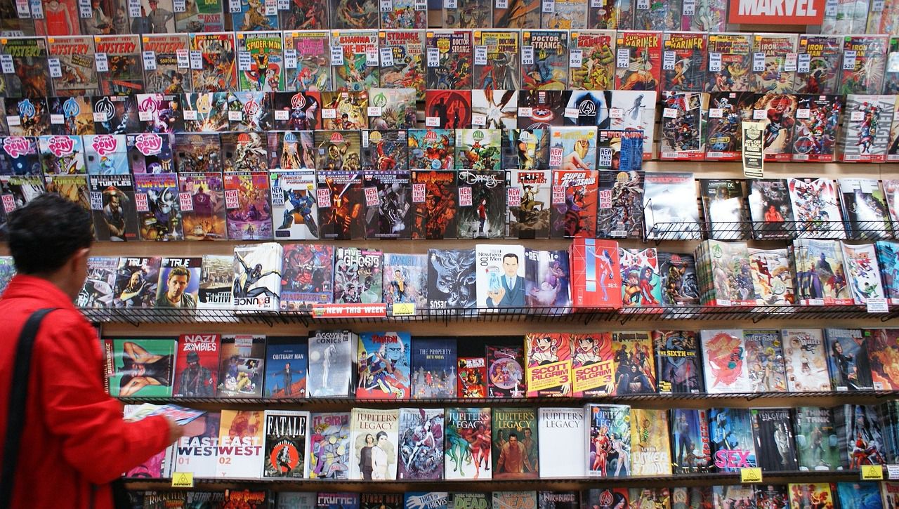 A person with short dark hair, wearing a red coat, stands in front of a wall displaying many different comic books
