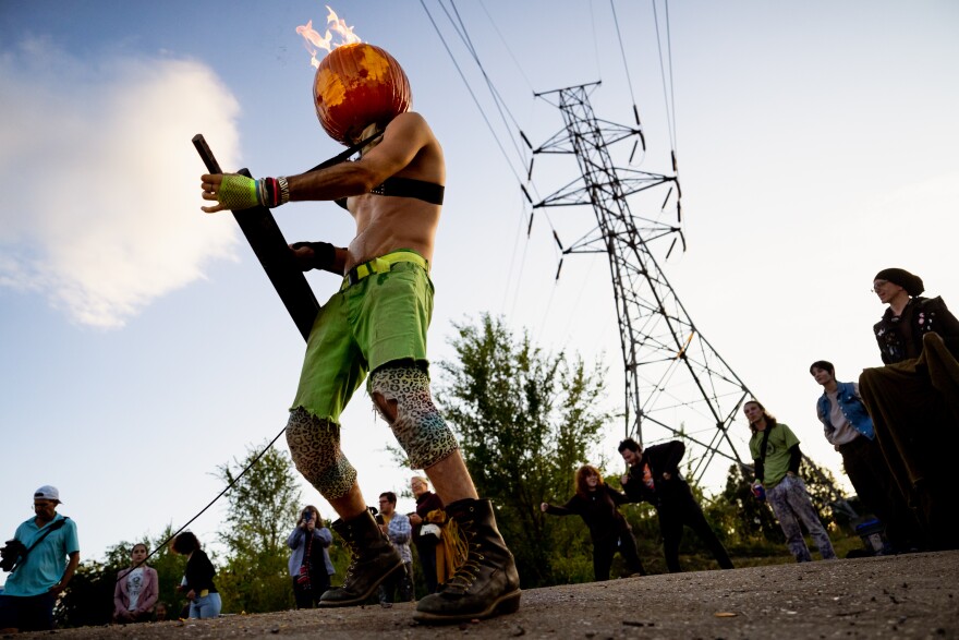 Kyle Kostecki, known as the persona “poopyknife,” lights up the keytar while wearing a pumpkin set ablaze by lighter fluid on Sunday, Oct. 8, 2023, during the Artica Urban Art Festival along the Mississippi Riverfront in downtown St. Louis.