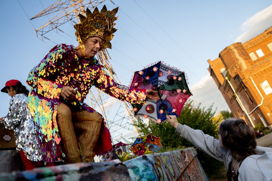 “Auntie Matthew,” who jokingly said was at least 16, of Tower Grove East, hands a parasol to Sophia Scuzzo, 13, of Affton, on Sunday, Oct. 8, 2023, during the Artica Urban Art Festival along the Mississippi Riverfront in downtown St. Louis. Matthew spent nearly 100 hours adding lights, scents, and more to the decorative fixtures.