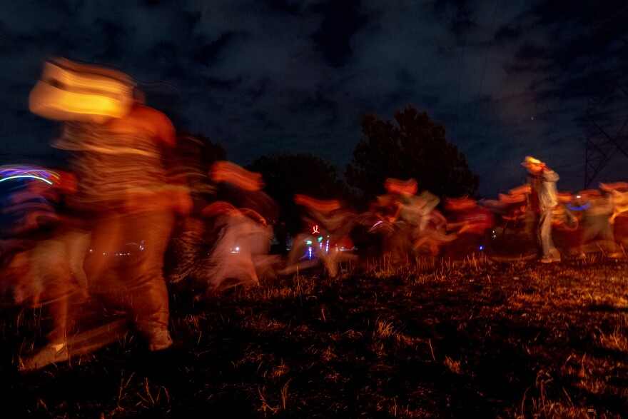Hundreds of festival goers dance and run around the burning ashes and embers of “Our Lady of Artica” on Sunday, Oct. 8, 2023, at the conclusion of the Artica Urban Art Festival held on the Mississippi Riverfront in downtown St. Louis.