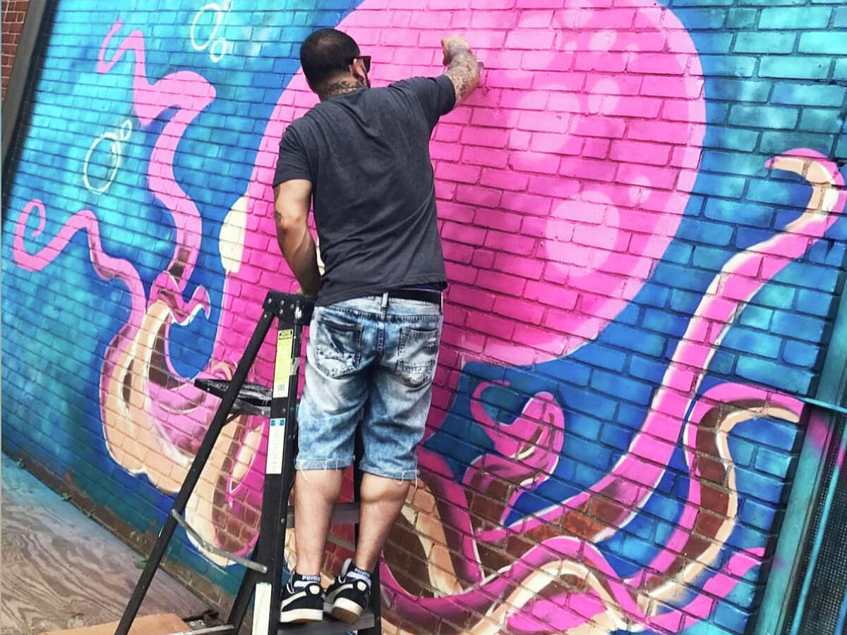Meriden artist, hairstylist and hip-hop musician Eddie Rivera recently completed a portion of a giant, floral-themed mural in the back alleyway of 418-20 Main St. in Middletown. He's shown here painting an octopus on a building in Meriden.