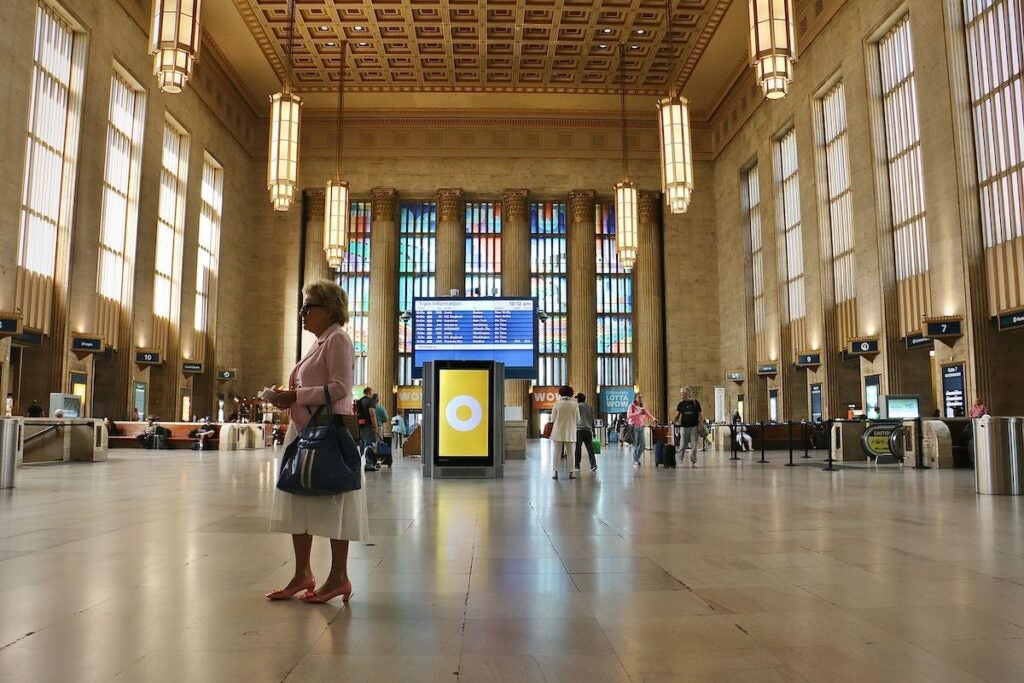 A woman waits for a train. Behind her is the artwork in the windows that is the latest addition to Amtrak 30th Street Station.