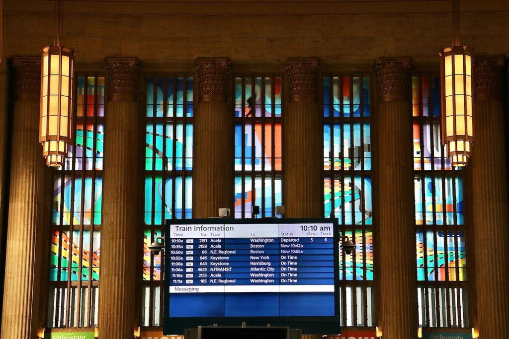 Panels of different colors are visible in the windows at Amtrak 30th Street Station. In the foreground is the train departure and arrival information board.