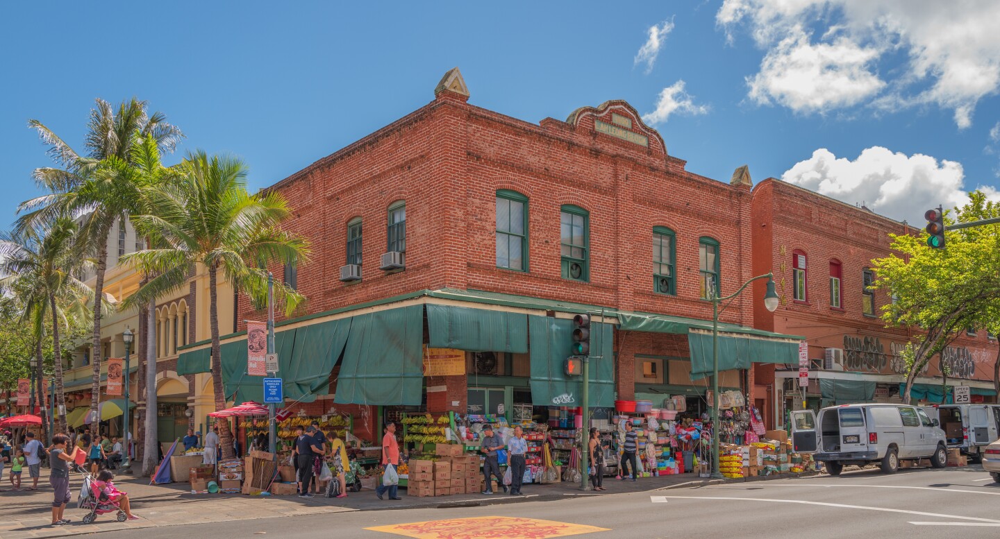 People shopping for groceries in front of a red brick building.