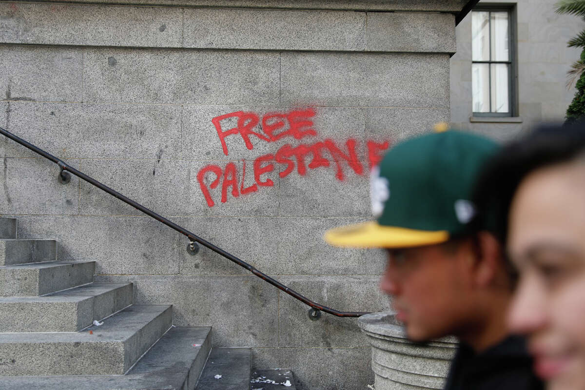People walk past graffiti reading “Free Palestine” that was written on the Old United States Mint building in San Francisco.