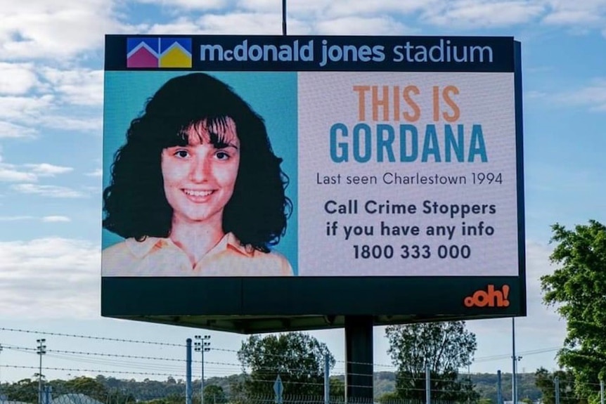 A billboard with Gordana's face on it next to writing 'this is Gordana last seen Charlestown 1994'