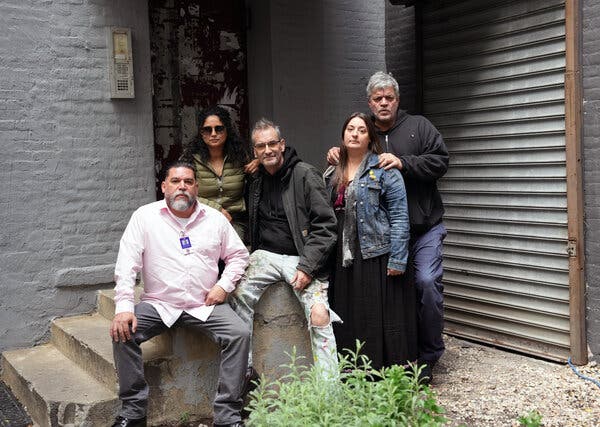 Five residents of a shuttered building pose while sitting and standing on concrete steps.