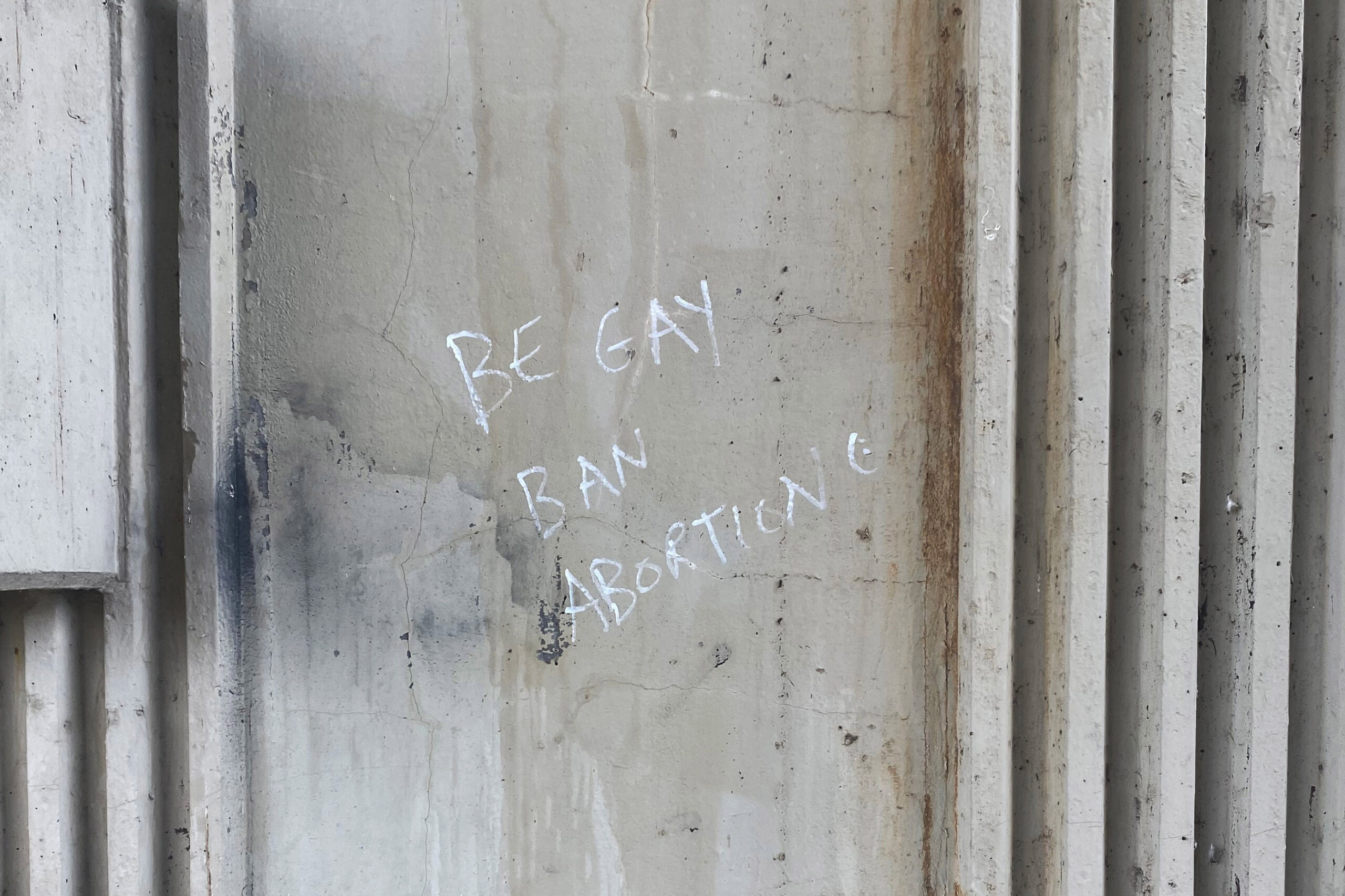 A photograph of graffiti written in white marker on a dilapidated wall. It reads, 