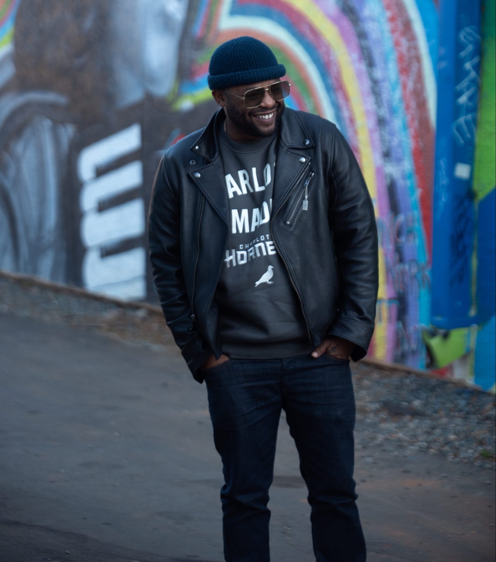 A photo of Mason Parker smiling with his hands in his pockets as he's posing in front of colorful artwork in the background.