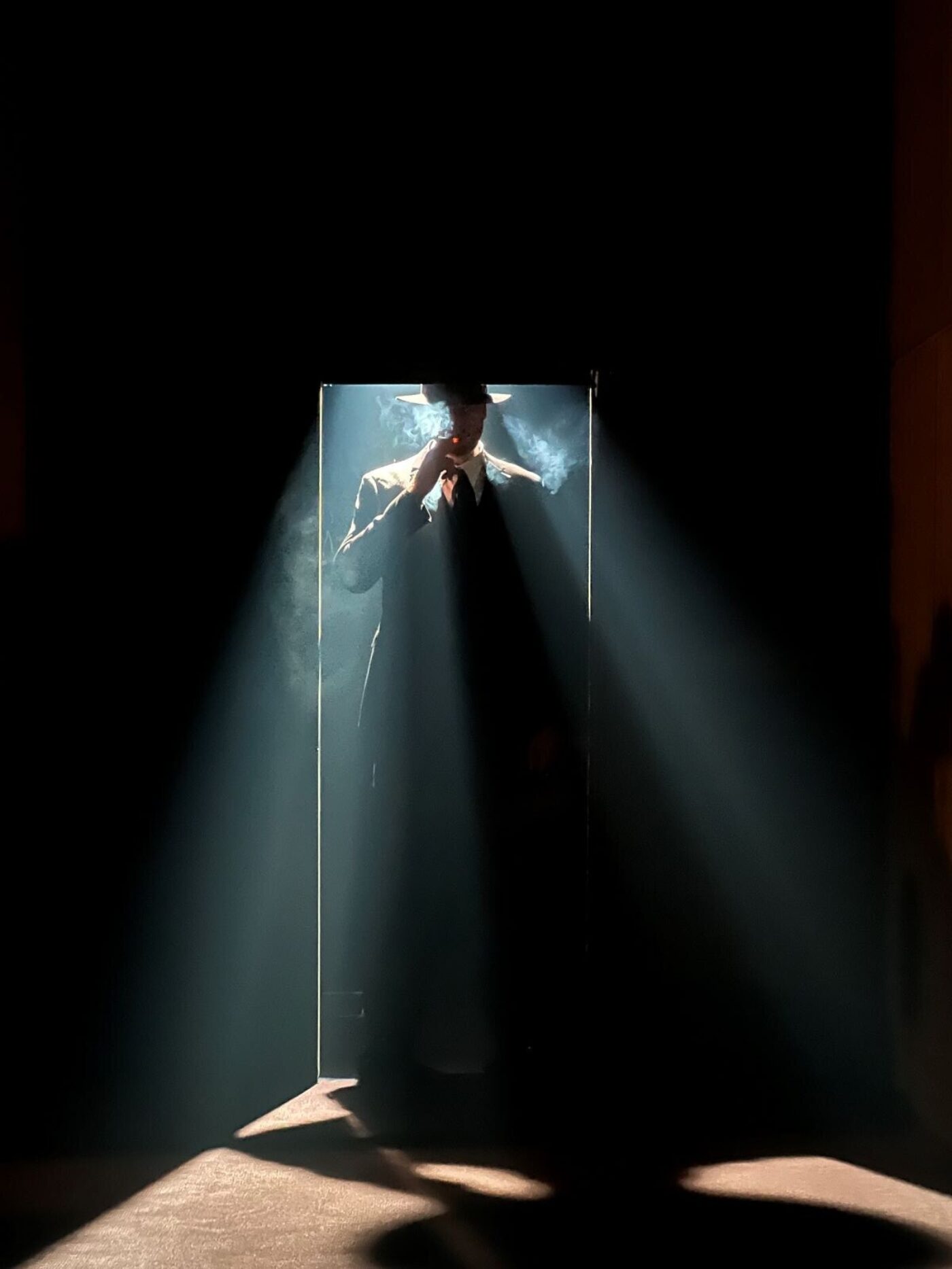 Onstage, a man in a hat is silhouetted as light pours through a doorway behind him.