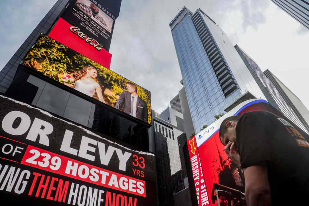 Michael Levy steht mit gesenktem Kopf während der Enthüllung einer digitalen Plakatwand am Times Square in New York, die Poster von Geiseln zeigt, die von der Hamas entführt wurden, darunter auch sein Bruder Or Levy. Foto: Bebeto Matthews/AP/dpa