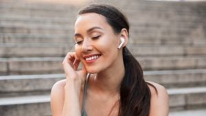 picture of woman with white earbuds listening to music while siting on stairs in an outdoor environment