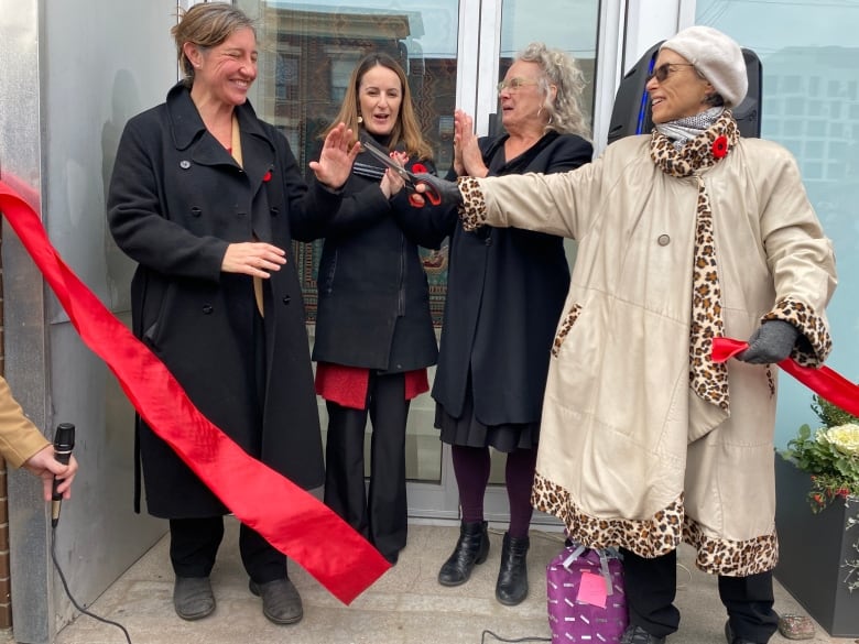 Four women laugh in front of a new building as a cut red ribbon flows in the wind.