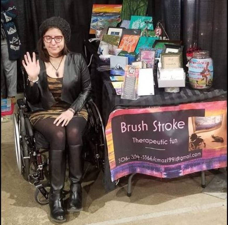 A woman in a wheelchair beside a table filled with artworks.