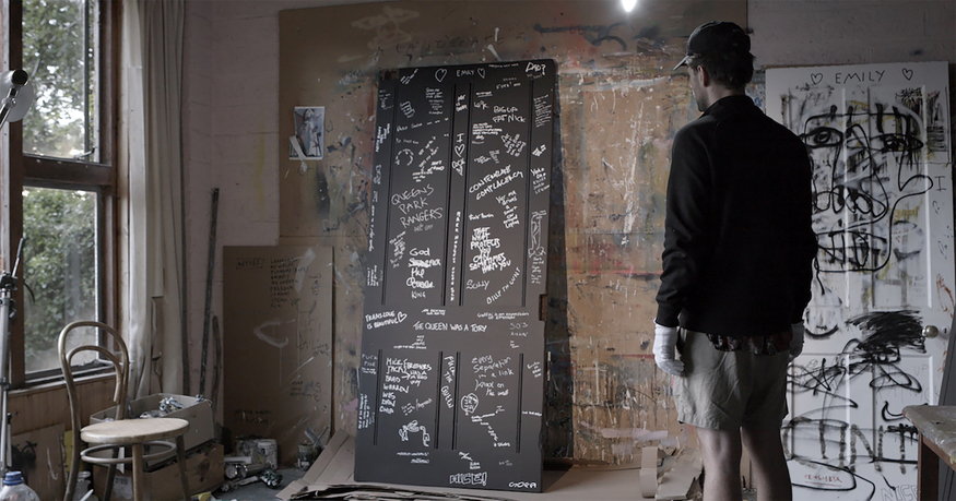 An artist in a studio looking at a graffitied door