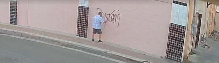 Surveillance footage shows a man in a checkered, light blue shirt spray-painting 