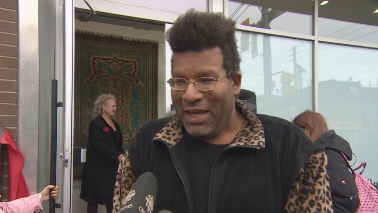 A young man speaks to a news reporter on camera. He is outside a building on a city street. it is cold and grey.