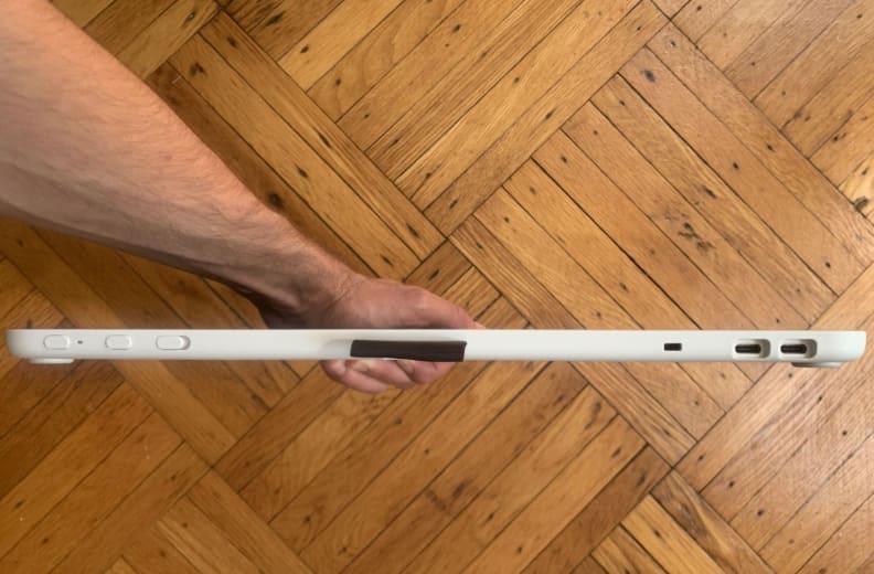 An arm holds the Wacom One over a wood floor, with its ports visible.