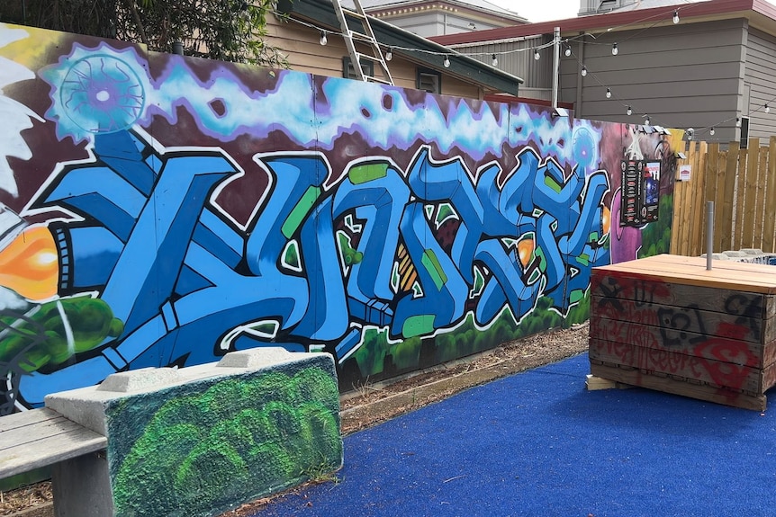 a blue eclectic artwork hangs on a fence