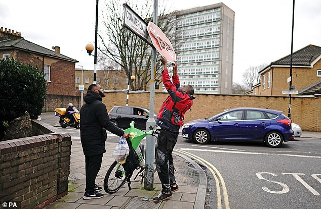 The man, dressed in a red jacket and apparently wearing work gear, pulls the sign down before making off with it