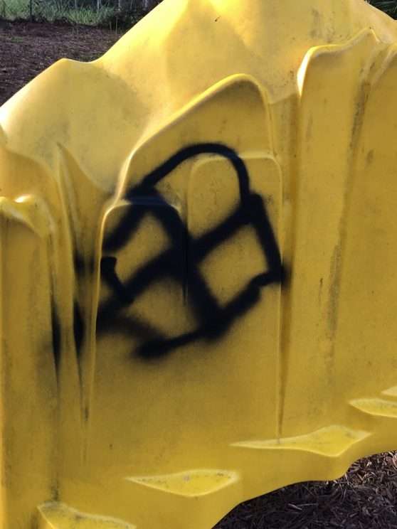yellow piece of playground equipment vandalized with Nazi graffiti 