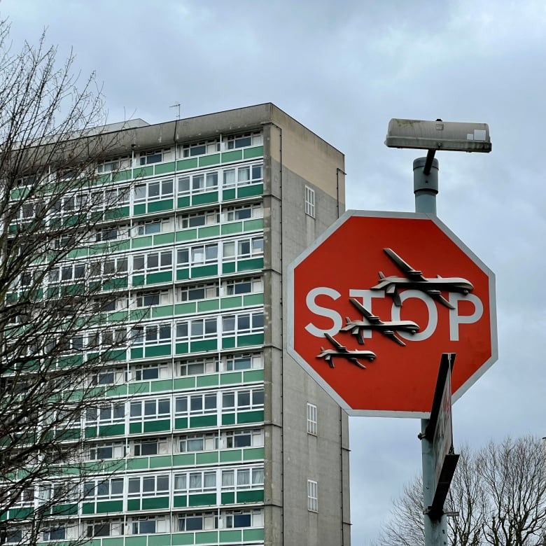 A stop sign adorned with artwork depicting military drones is seen.