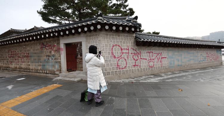 A pedestrian takes photos of  graffiti that reads 