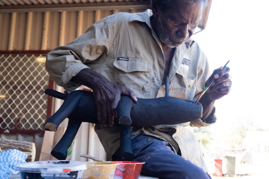 A man paints the mouth of a black wooden dog sculpture.