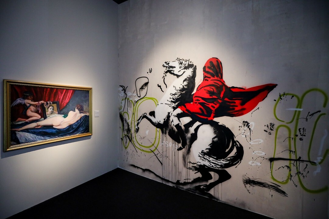 A Banksy mural featuring a red-cloaked figure on a horse in a gallery space.