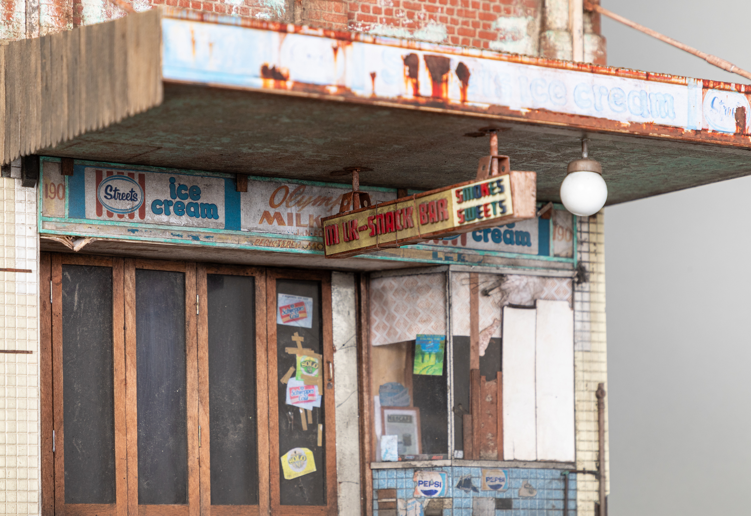 Detail of a miniature model of a storefront, focused on a rusted awning and old signage with letters faded and missing.