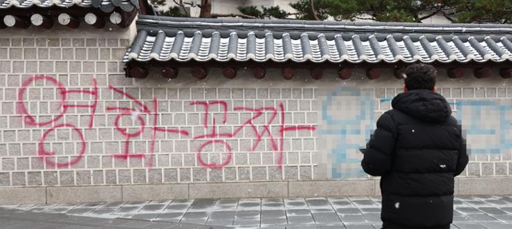 A pedestrian stands in front of  red and blue graffiti that reads 'free movie' spray-painted on a wall of Gyeongbok Palace in central Seoul, Dec. 16, 2023. Yonhap
