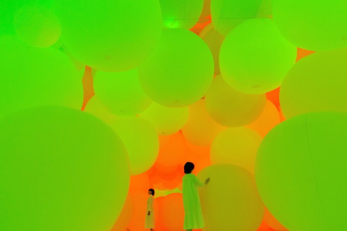 Two women walk among large glowing spheres in a gallery