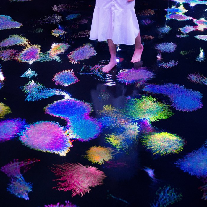 A woman walks across a floor that has colourful geometric shapes projected on to it